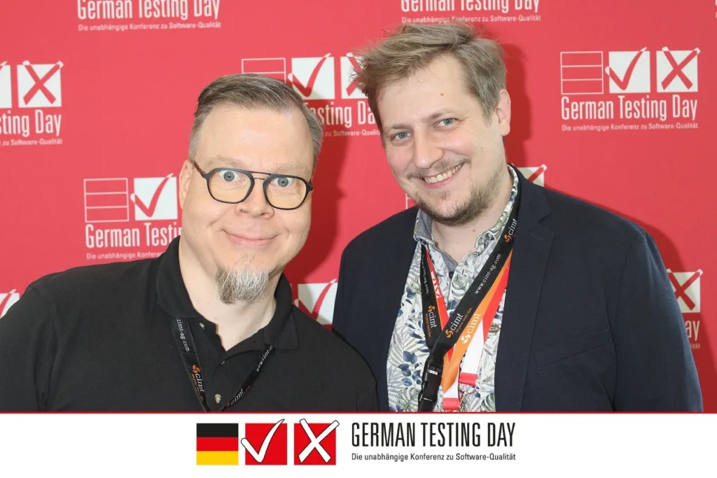 Oliver Schuhmacher (links) und Marvin (rechts) beim German Testing Day 2025 vor der Veranstaltungswand.